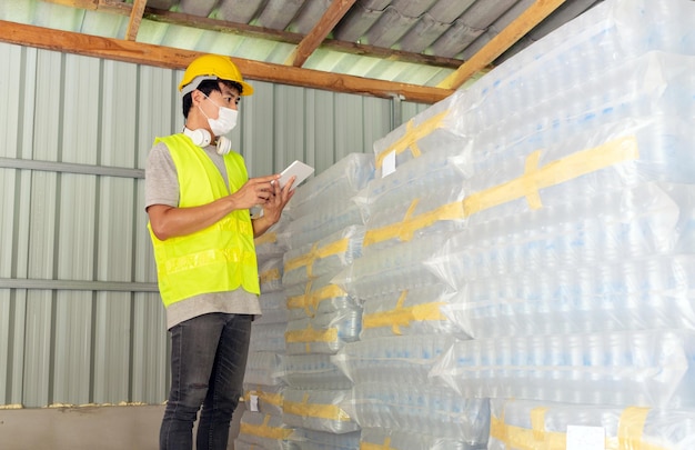 Un trabajador revisando el stock de botellas de plástico en el almacén usando una tableta para actualizar en línea