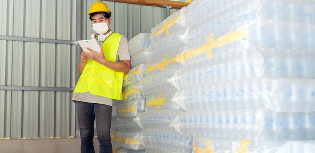 trabajador revisando el stock de botellas de plástico en el almacén usando una tableta para actualizar el stock en línea