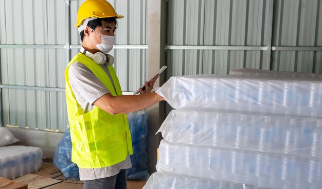 trabajador revisando el stock de botellas de plástico en el almacén usando una tableta para actualizar el stock en línea