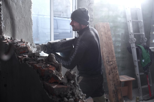 Un trabajador rompe una pared de ladrillos con un martillo neumático, construye y repara su casa.