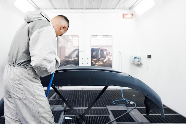 Trabajador en ropa de trabajo protectora aplica pintura en el parachoques del automóvil