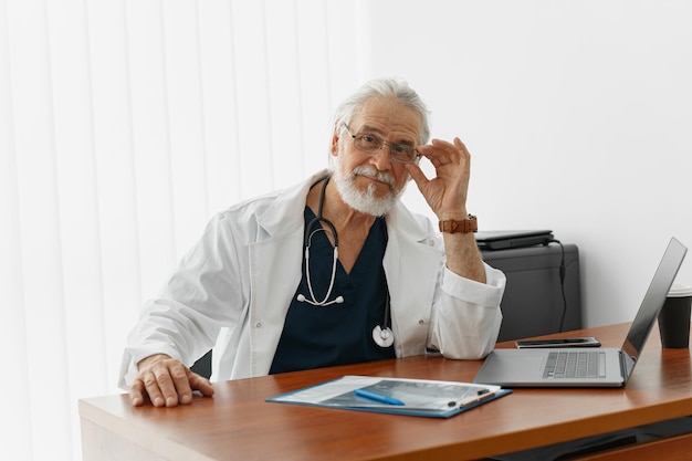 Foto trabajador de la salud de alto nivel haciendo papeleo y usando una computadora portátil mientras trabaja en la oficina de doctor39s