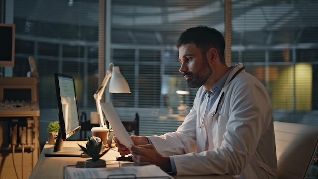 Trabajador sanitario analizando registros por la noche En primer plano el escritorio de trabajo del médico molesto