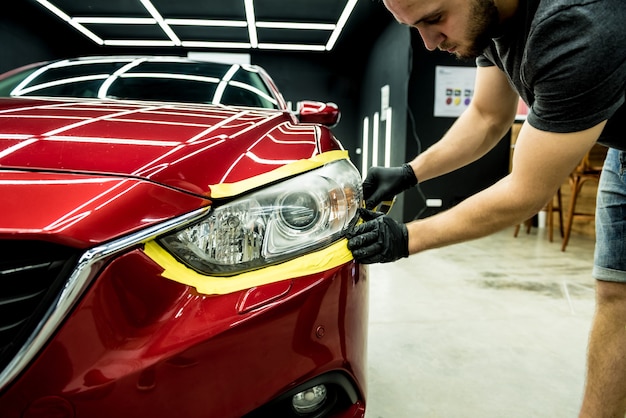 Trabajador de servicio de automóvil aplicando cinta protectora en los detalles del automóvil antes de pulir.