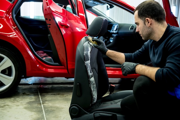 Trabajador de servicio de automóvil limpia un asiento de automóvil con un cepillo especial