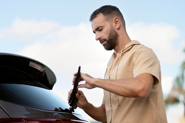 El trabajador del servicio de automóviles pensativo reemplaza los limpiaparabrisas en el automóvil parado al aire libre