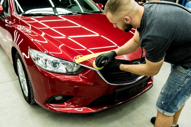 El trabajador del servicio de automóviles pule los detalles de un automóvil con un pulidor orbital.