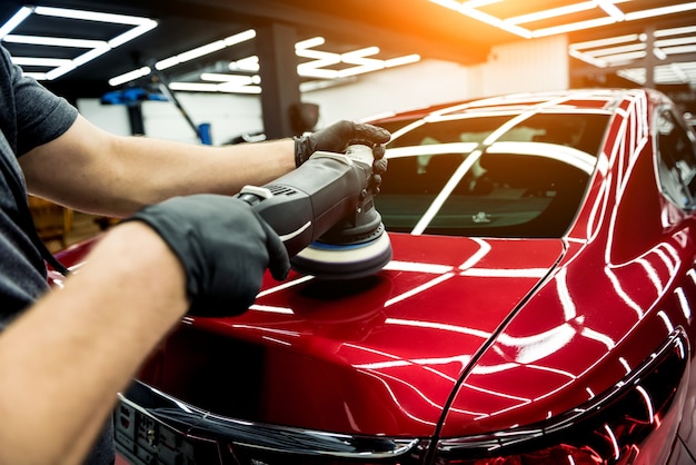 Foto el trabajador del servicio de automóviles pule los detalles de un automóvil con un pulidor orbital.