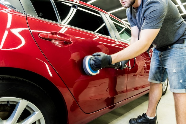 El trabajador del servicio de automóviles pule los detalles de un automóvil con un pulidor orbital.