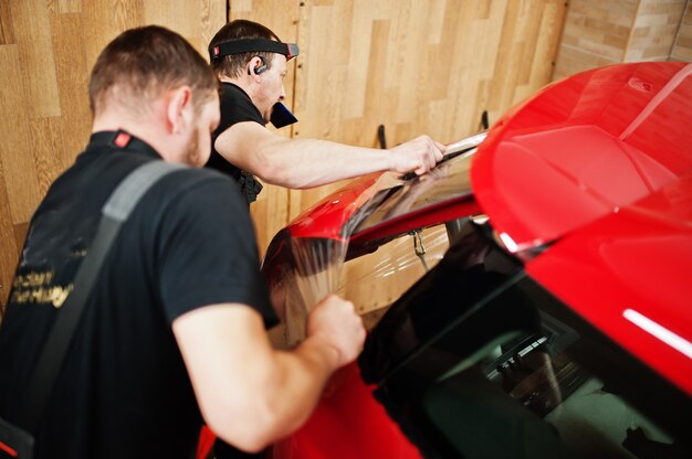 El trabajador del servicio de automóviles puso una película anti-grava en la carrocería de un automóvil rojo en el taller de detalle del vehículo