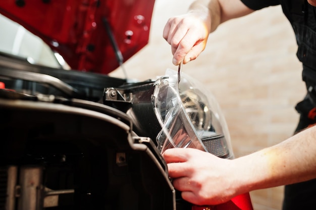 El trabajador del servicio de automóviles puso una película antigravilla en una carrocería de automóvil roja en el taller de detalles de vehículos Protección de automóviles con películas especiales