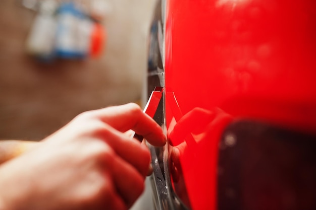 El trabajador del servicio de automóviles puso una película antigravilla en una carrocería de automóvil roja en el taller de detalles de vehículos Protección de automóviles con películas especiales