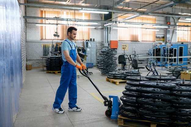 Trabajador de sexo masculino lleva ruedas de bicicleta en un carro en la fábrica. Línea de montaje de llantas de bicicleta en taller, instalación de piezas de ciclo, tecnología moderna