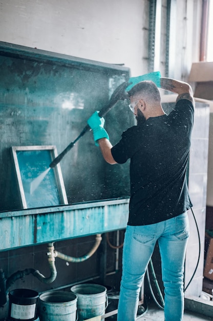 Trabajador de sexo masculino que limpia el marco de la pantalla con agua en un taller de impresión