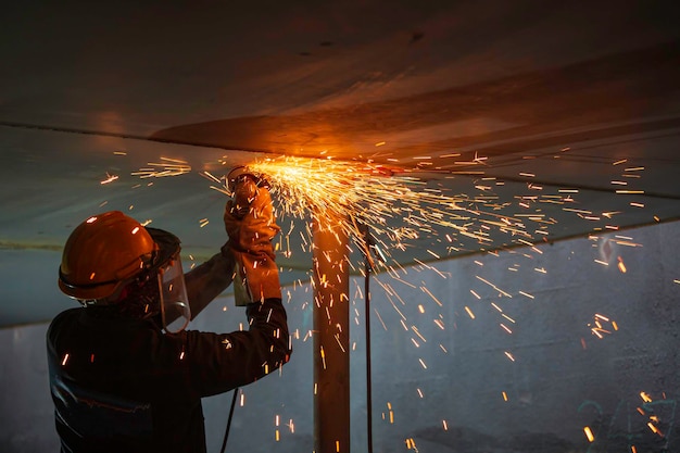 Trabajador de sexo masculino que usa la chispa de la rueda eléctrica en la placa del techo de la pieza de acero al carbono del soldador dentro del espacio confinado del tanque