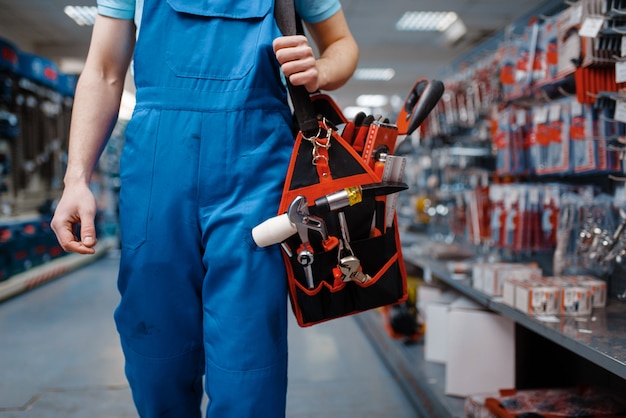 Trabajador de sexo masculino en uniforme tiene caja de herramientas en la tienda de herramientas. Elección de equipos profesionales en ferretería, supermercado de instrumentos