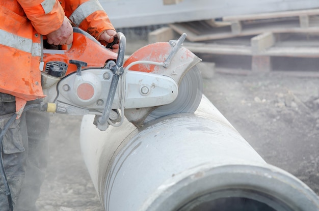Un trabajador en el sitio de construcción cortando una tubería de drenaje de hormigón con una sierra de hormigón