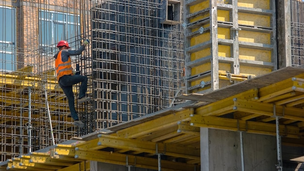 Trabajador en el sitio de construcción de rascacielos empleado hombre en el chaleco naranja