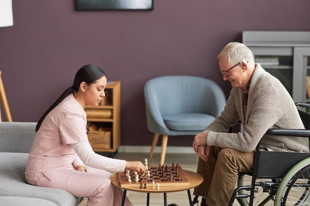 Trabajador social jugando al ajedrez con un anciano