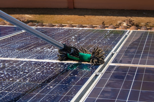 Trabajador solar limpiando paneles fotovoltaicos con cepillo y agua. Limpieza fotovoltaica.