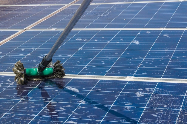 Trabajador solar limpiando paneles fotovoltaicos con cepillo y agua