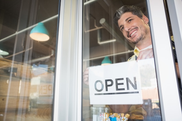 Foto trabajador sonriente que pone el cartel abierto