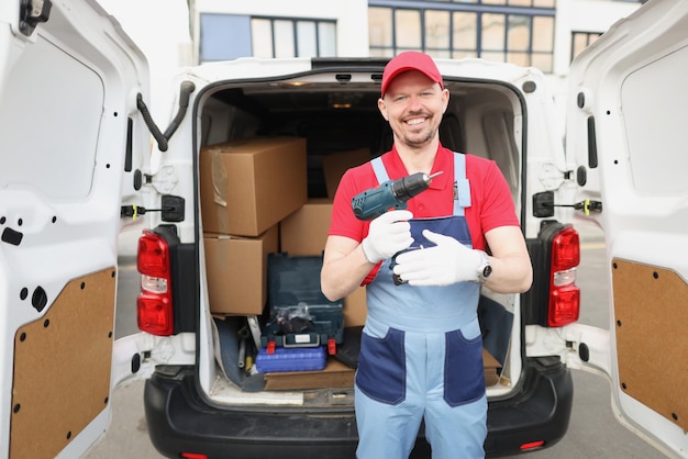 Trabajador sonriente sostenga el dispositivo destornillador en la mano frente al camión lleno de cajas