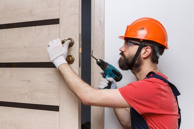 Un trabajador con un taladro en un casco naranja instala una puerta en la casa