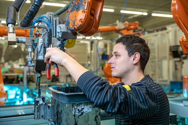 Foto trabajador técnico realiza mantenimiento de brazos robóticos en la línea de producción