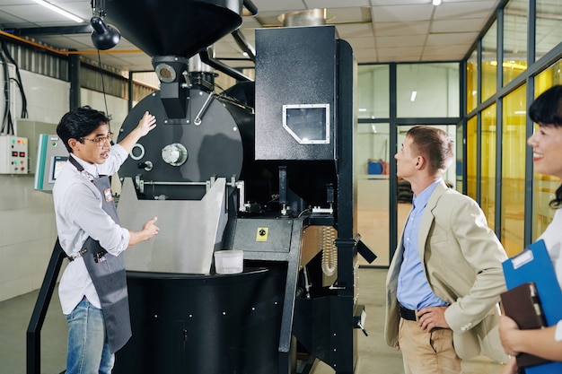Trabajador tostador de café mostrando nueva máquina al inversor y hablando de sus beneficios