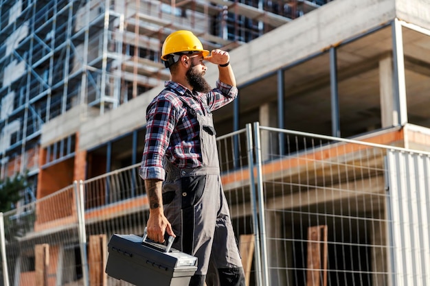 Un trabajador trabajador con una caja de herramientas en la mano llega a un sitio de construcción