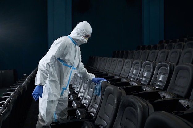 Trabajador en traje especial limpiando sillas trapo en la sala de cine.