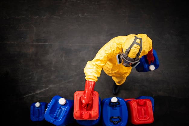 trabajador con traje protector de materiales peligrosos que trabaja dentro de una fábrica de productos químicos que mueve botes o tanques de plástico