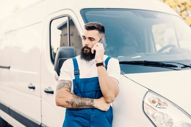 Un trabajador del transporte apoyado en la camioneta y hablando por teléfono con el cliente