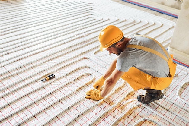 Trabajador en uniforme de color amarillo instalando sistema de calefacción por suelo radiante