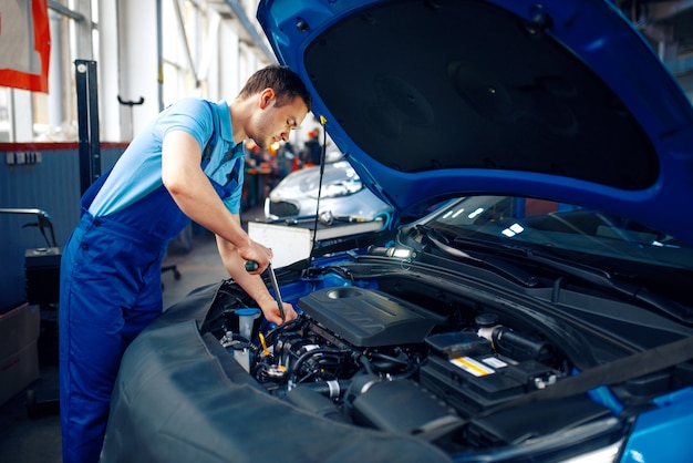 Trabajador en uniforme comprueba el motor del vehículo, la estación de servicio del coche. Comprobación e inspección de automóviles, diagnóstico y reparación profesionales