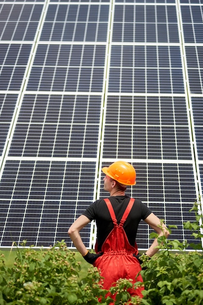 Trabajador con uniforme naranja se para de espaldas a la cámara contra el fondo de grandes baterías solares de plantación