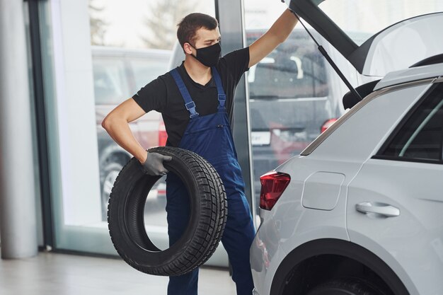 Trabajador en uniforme negro y azul con rueda de coche y trabajo en interiores