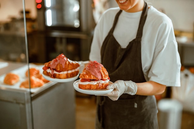 Trabajador en uniforme sostiene sabrosos croissants con relleno en panadería artesanal closeup