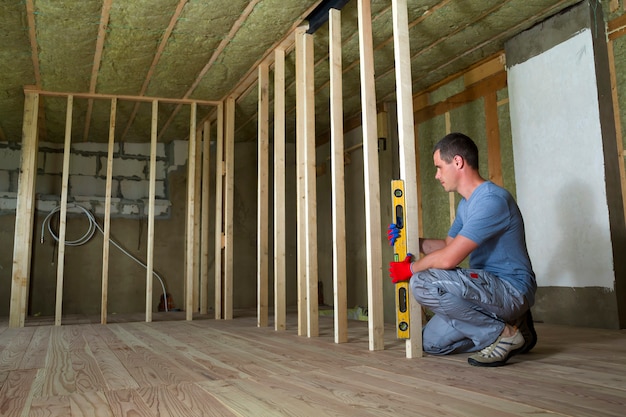 El trabajador usa el nivel instalando el marco de madera para paredes futuras.