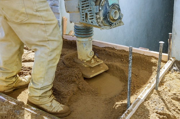 Trabajador utiliza compactador para herramienta eléctrica vibratoria en el suelo en la construcción del sitio de trabajo nueva acera