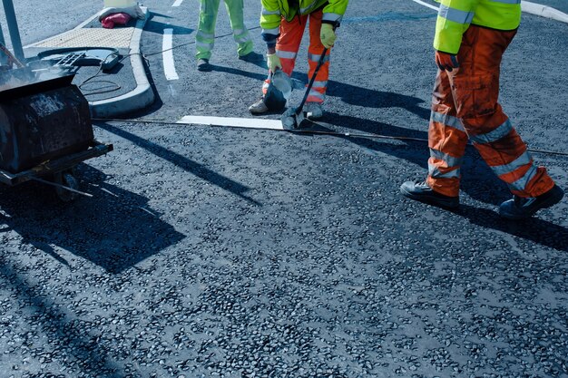 Trabajador vial aplicando señalización vial termoplástica en el asfalto recién colocado durante la nueva rotonda y construcción de carreteras de acceso