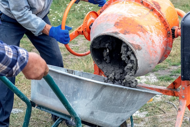 Un trabajador vierte hormigón de mortero de cemento de una hormigonera en una carretilla Preparación de mortero de cemento en el sitio de construcción