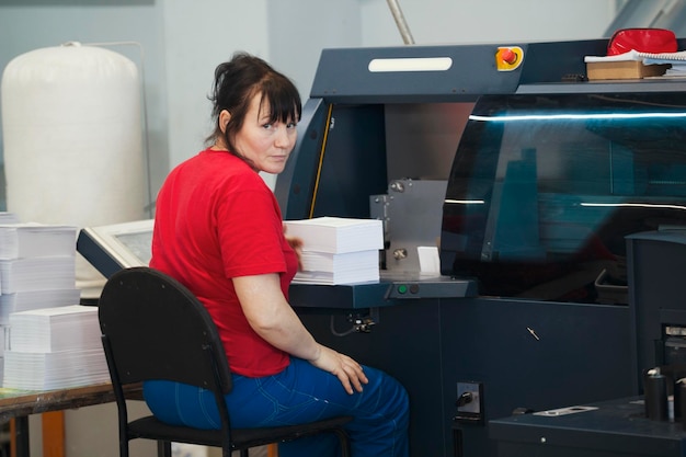 Trabajadora adulta con pilas de papel frente al equipo de imprenta