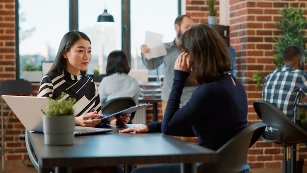 Trabajadora asiática saludando a una candidata en una entrevista de trabajo para discutir la oferta de trabajo y la oportunidad de carrera. Reclutador de recursos humanos mirando cv y entrevistando a una mujer en la reunión de contratación.