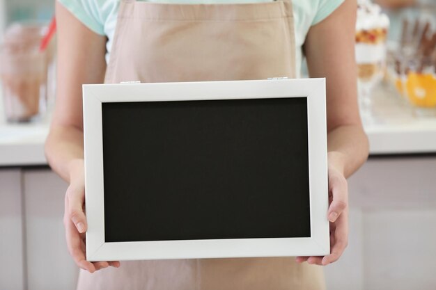 Trabajadora de la barra de leche femenina sosteniendo una pizarra negra sobre fondo borroso