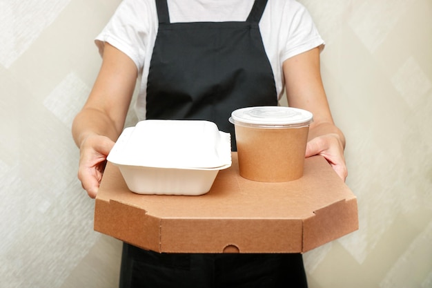 Foto una trabajadora de cafetería sirve un pedido para llevar completo, pizza en caja y un recipiente con aperitivos y sopa en utensilios desechables hechos de materias primas recicladas.