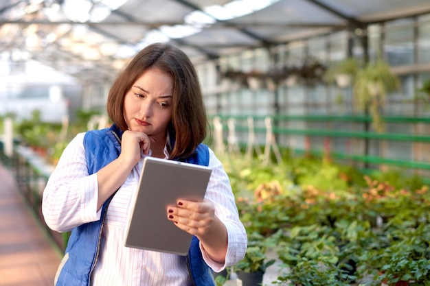 Trabajadora con catálogo de flores tableta en línea en invernadero Concepto de trabajo en plantas de invernadero