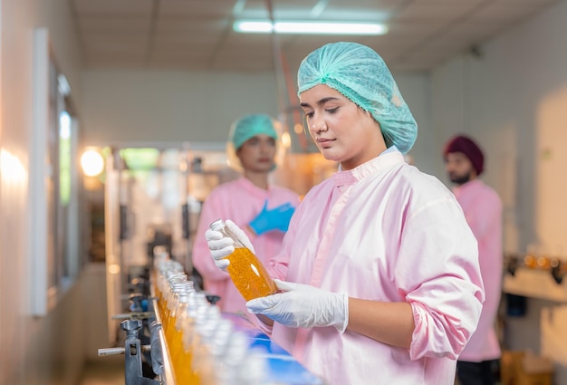 Trabajadora comprobando la calidad de la botella de bebida de jugo de frutas en la línea de producción de la fábrica de bebidas