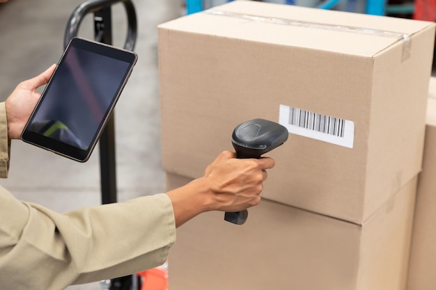 Trabajadora escaneando un paquete con escáner de códigos de barras mientras usa una tableta digital en el almacén